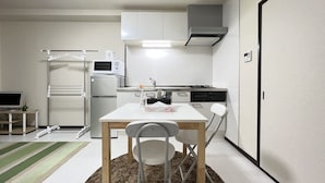A compact kitchen with white cabinets, a microwave, a refrigerator, and a dining area with a table and chairs. - Gojo sefi-apartment 101 (Kyoto)