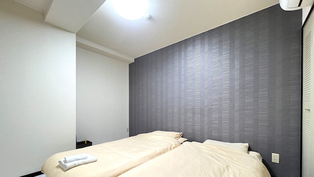 A hotel room with two beds, a grey textured wall, and a ceiling light. - Gojo sefi-apartment 101 (Kyoto)