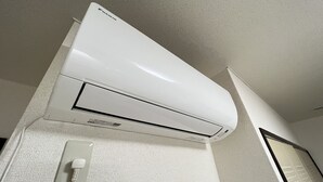 A white air conditioning unit mounted on a textured wall with a power outlet below it. - Gojo sefi-apartment 101 (Kyoto)
