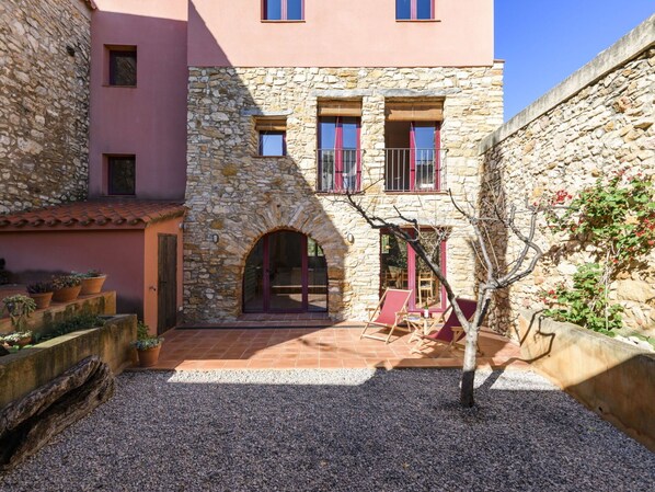 Un patio con un edificio de piedra, un banco de madera y plantas en macetas.