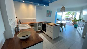 Una cocina moderna con encimera de madera, armarios blancos y vistas a un área de comedor con mobiliario exterior.