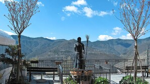 A statue of a figure with a staff, surrounded by a metal fence, benches, and potted plants, with a mountainous backdrop. - Stunning  villa for 6 guests with WIFI and TV (Molini Di Triora)