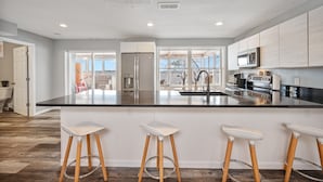 A modern kitchen with a large island, stainless steel appliances, and wooden stools. - Beautiful Sunrise Views of Hall Lake! (Fairmont)