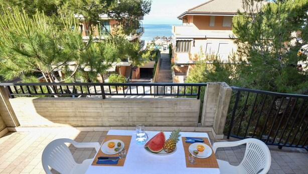 A table set on a balcony with a view of the sea, two white plastic chairs, and a tablecloth. - Nice apartment for 3 people with WIFI, TV, terrace and pets allowed (Silvi)