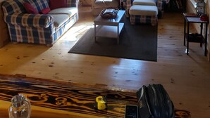 A cozy cabin interior with a wooden floor, a sofa set, a chair, a small table, and a bookshelf.