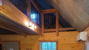 A wooden cabin interior with a dining table, a window with a view of trees, and an air conditioning unit.