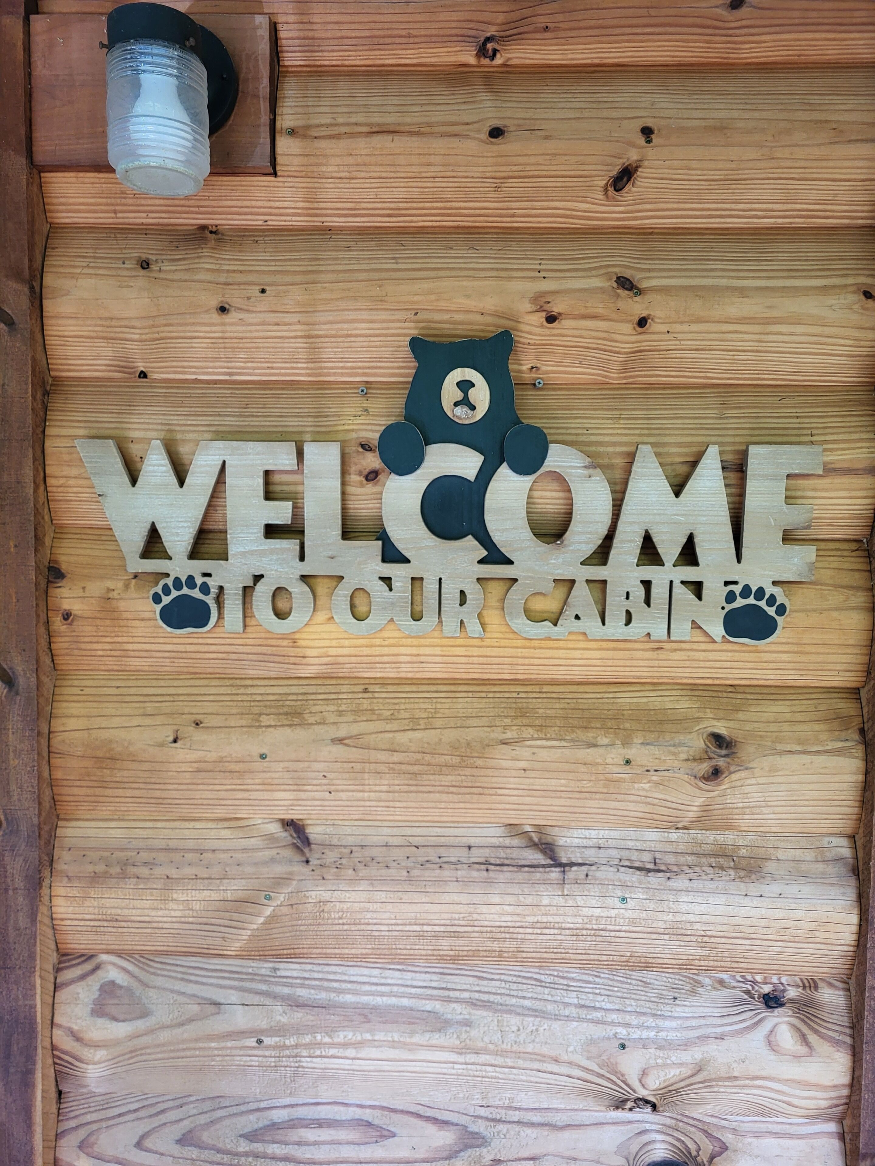 A wooden cabin door with a bear cutout and the words "WELCOME TO OUR CABIN" in large letters.