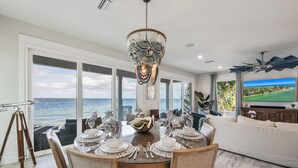 Een eetruimte met uitzicht op zee, een kroonluchter en een televisie waarop een golfbaan te zien is.