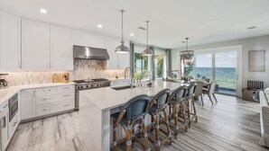 Een moderne keuken met witte kasten, een groot eiland met barkrukken en uitzicht op de oceaan.