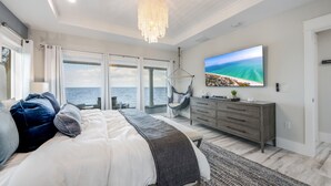 Een slaapkamer met een groot bed, een kroonluchter, een televisie en uitzicht op de oceaan.
