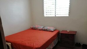 A bedroom with a bed, a nightstand, a window, and a chair.