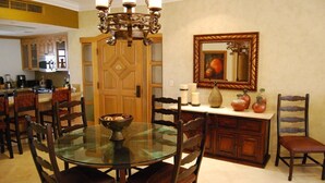 Un coin repas avec une table en verre entourée de chaises en bois, un lustre, un buffet en bois et un miroir au mur.