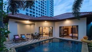 A modern pool area with a tiled floor, a seating area with chairs and a table, and a glass-enclosed room with a bed. - AnB poolvilla 2BR with private beach (Pattaya)