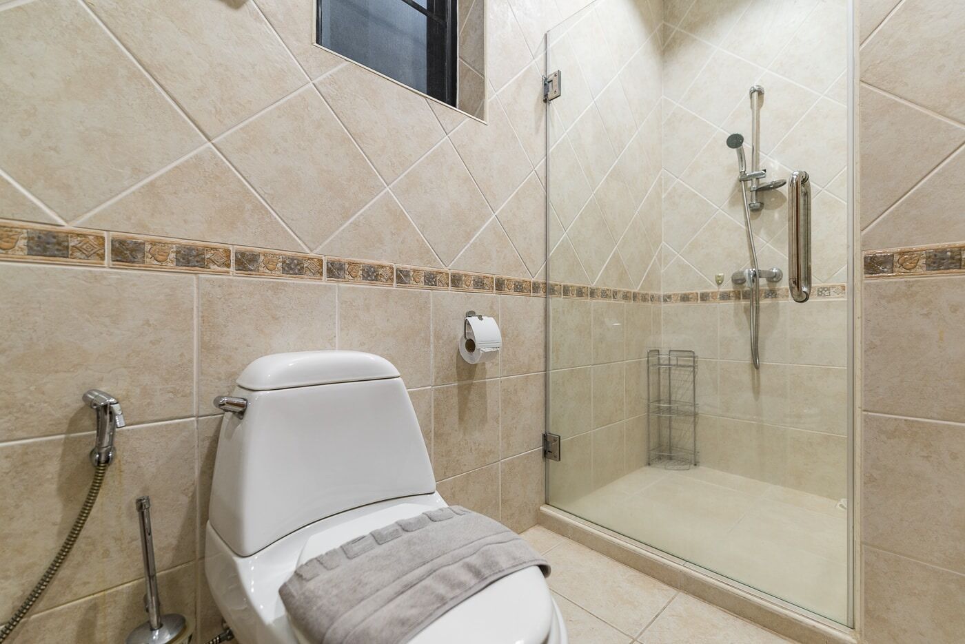Un baño con inodoro, ducha con puerta de vidrio y una toalla en el suelo.