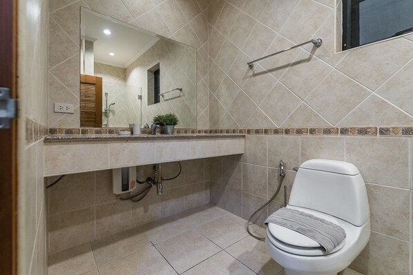 A bathroom with a toilet, a sink with a mirror, and a shower area.
