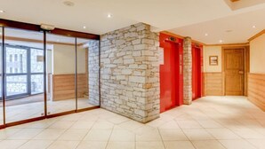 Un vestíbulo de hotel espacioso con una pared de piedra, ascensores rojos y un gran ventanal que da a un balcón.