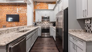 A modern kitchen with granite countertops, stainless steel appliances, and a brick accent wall. - ⚜️ Perfect Downtown 1 Bedroom plus Queen Sleeper Sofa & Private Terrace ⚜️ - The Livingston (New Orleans)