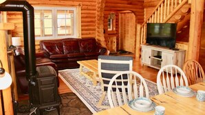 L’intérieur d’une cabane en rondins, avec un escalier en bois, un canapé en cuir, une table à manger et un téléviseur.