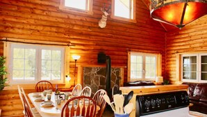 L’intérieur d’un chalet en bois, avec une table à manger dressée pour quatre personnes, un poêle et une cheminée.
