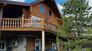 Une cabane en rondins dotée d’un balcon, d’un espace extérieur aménagé et d’un grand arbre à proximité.