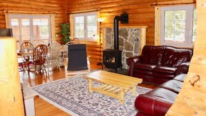 L’intérieur d’une cabane en rondins, avec une cheminée en pierre, des meubles en bois et de grandes fenêtres.