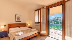 Een slaapkamer met een houten bed, nachtkastje, uitzicht op een balkon met een hekwerk, en een raam met gordijnen.