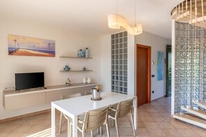 A modern kitchen with a dining area, a TV, and decorative items on the wall. - Albarella S3 1, Isola di Albarella, Italy (Isola di Albarella)