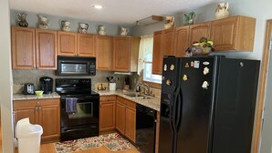Una cocina compacta con armarios de madera, un refrigerador negro, un microondas, una estufa y una cafetera.