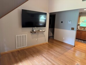 A room with a mounted flat-screen TV, a built-in heater, and a wooden floor.
