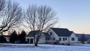 Ein zweistöckiges Haus mit dunklem Dach und weißer Fassade, umgeben von schneebedecktem Boden und kahl stehenden Bäumen.