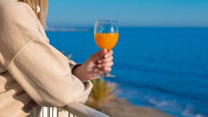 Iemand houdt een glas sinaasappelsap vast, met op de achtergrond een strand en de oceaan.
