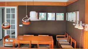 Een eetruimte met een houten tafel en stoelen, een hanglamp en kunstwerken in lijsten aan de muur.