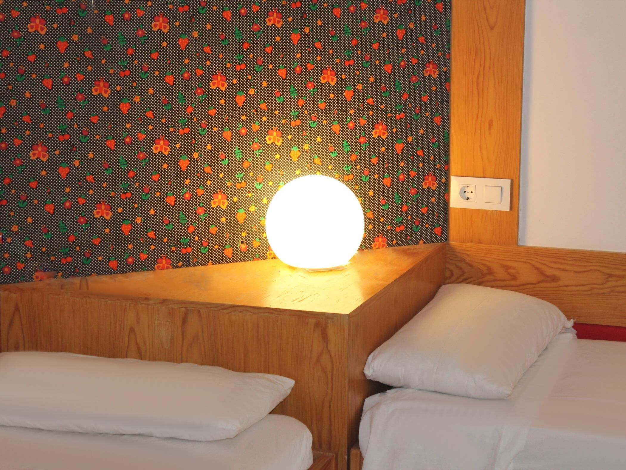 Et hotelværelse med en trægavl, en væg med et farverigt mønster og en sengebordlampe.