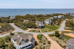 An aerial view of a coastal residential area with houses, a curved road, and a body of water in the background.