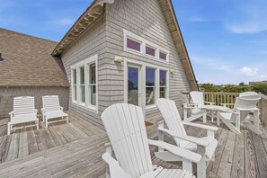 A wooden deck with Adirondack chairs and a building with large windows.