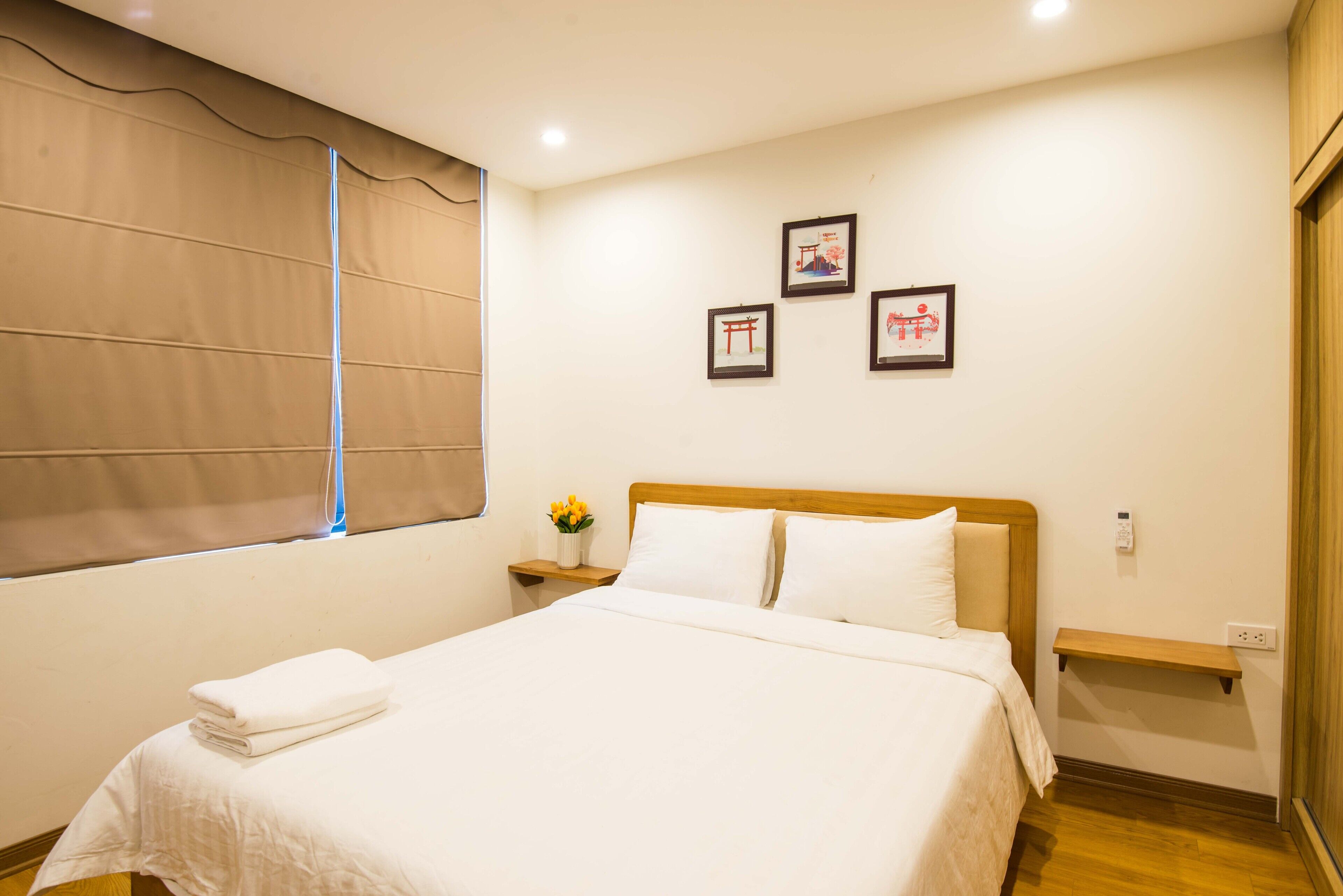 A neatly made bed with white linens, a bedside table with a vase of yellow flowers, and three framed pictures on the wall.