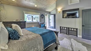 Un dormitorio con una cama, un aparador, un ventanal, un televisor y una puerta.
