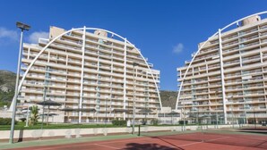 Ein Tennisplatz mit zwei großen, modernen Wohngebäuden im Hintergrund.
