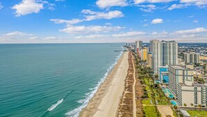 A coastal cityscape with a beach, high-rise buildings, and a clear sky.
