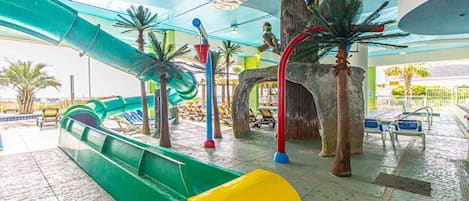 An indoor water park with slides, palm trees, and lounge chairs.
