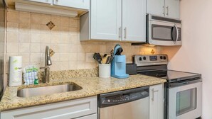 A kitchen with white cabinets, a granite countertop, a dishwasher, an oven, and a microwave. - Towers On the Grove 724 (North Myrtle Beach)