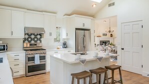 A modern kitchen with white cabinetry, stainless steel appliances, and a central island with stools. - Secluded Luxury Haven | Hot Tub, Billiards, Firepit & Spa Ambiance near Beach (Montecito)