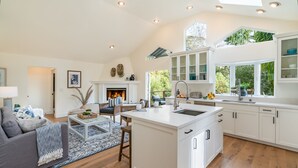 A modern kitchen with white cabinetry, a central island, and a large window overlooking greenery. - Secluded Luxury Haven | Hot Tub, Billiards, Firepit & Spa Ambiance near Beach (Montecito)