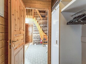 Interior de madeira com escada que leva a um loft, piso de azulejos brancos e um eletrodoméstico branco à direita.