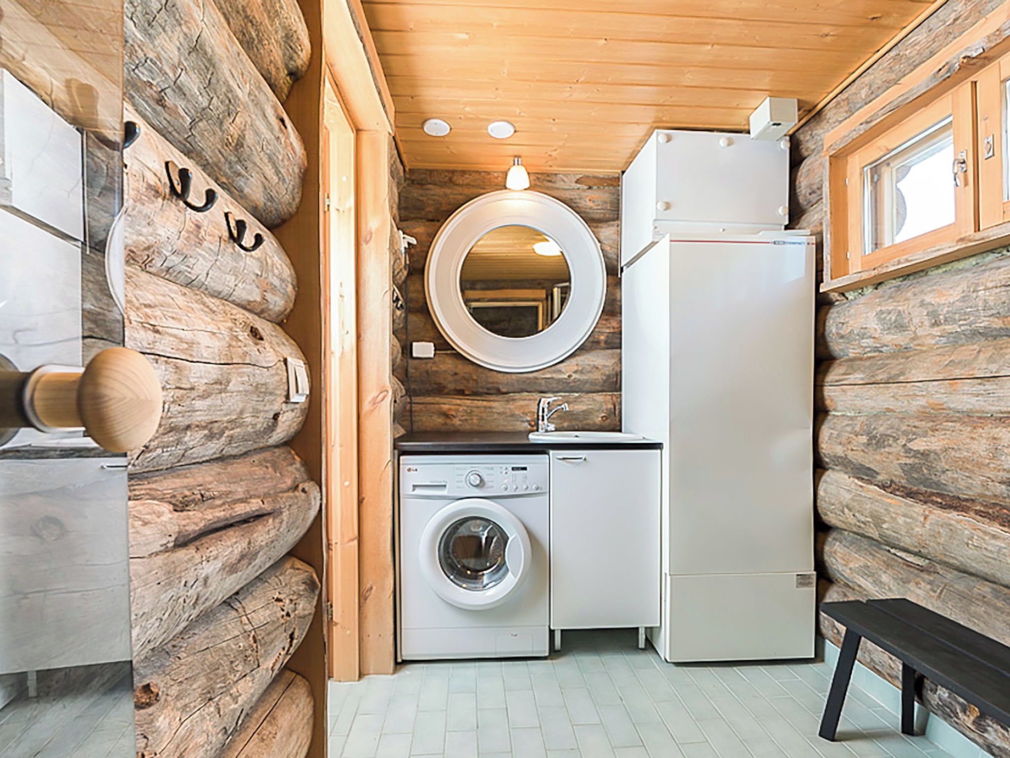 A compact kitchen with a washing machine, a refrigerator, and wooden log walls.
