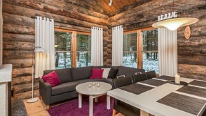 L'intérieur d'une cabane en rondins, avec un canapé, une table à manger et de grandes fenêtres.