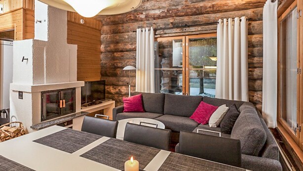 L’intérieur d’une cabane en rondins, avec une cheminée, un canapé, une table à manger et un grand luminaire suspendu.