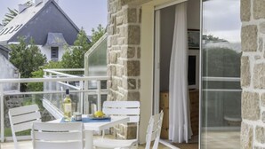 A balcony with white chairs and a table, a stone wall, and a sliding glass door leading to a room. - Le Hoche by Interhome (Quiberon)