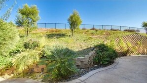 Un jardín ajardinado con un muro de piedra, un sendero curvo y una valla de metal al fondo.