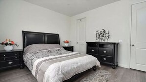 Un dormitorio con cama, mesitas de noche, cómoda y puerta.